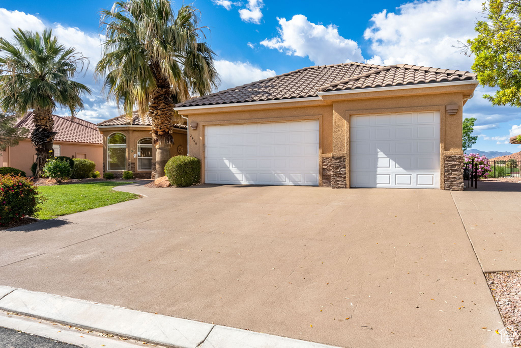 Mediterranean / spanish-style home featuring stucco siding, driveway, a tiled roof, stone siding, and a garage