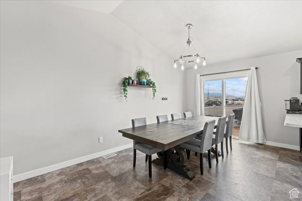 Dining space with stone finish floor, visible vents, vaulted ceiling, baseboards, and a notable chandelier