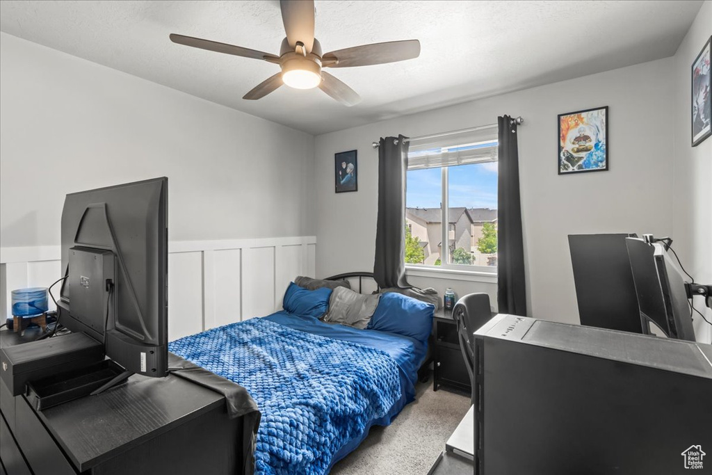 Carpeted bedroom featuring ceiling fan and a wainscoted wall