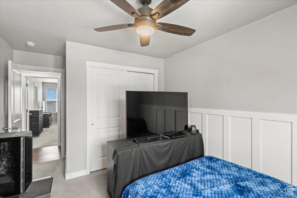 Carpeted bedroom featuring a closet, wainscoting, and a ceiling fan