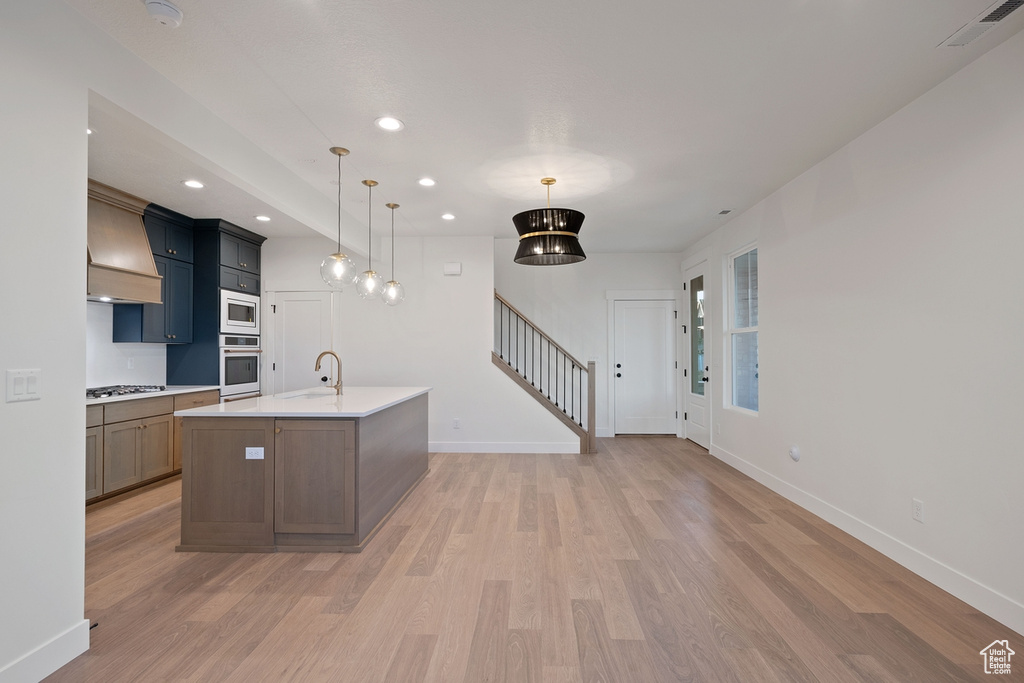 Kitchen with white oven, built in microwave, gas cooktop, a sink, and light wood-style flooring