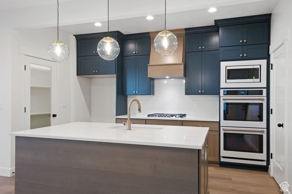 Kitchen with white double oven, a sink, built in microwave, gas cooktop, and wood finished floors