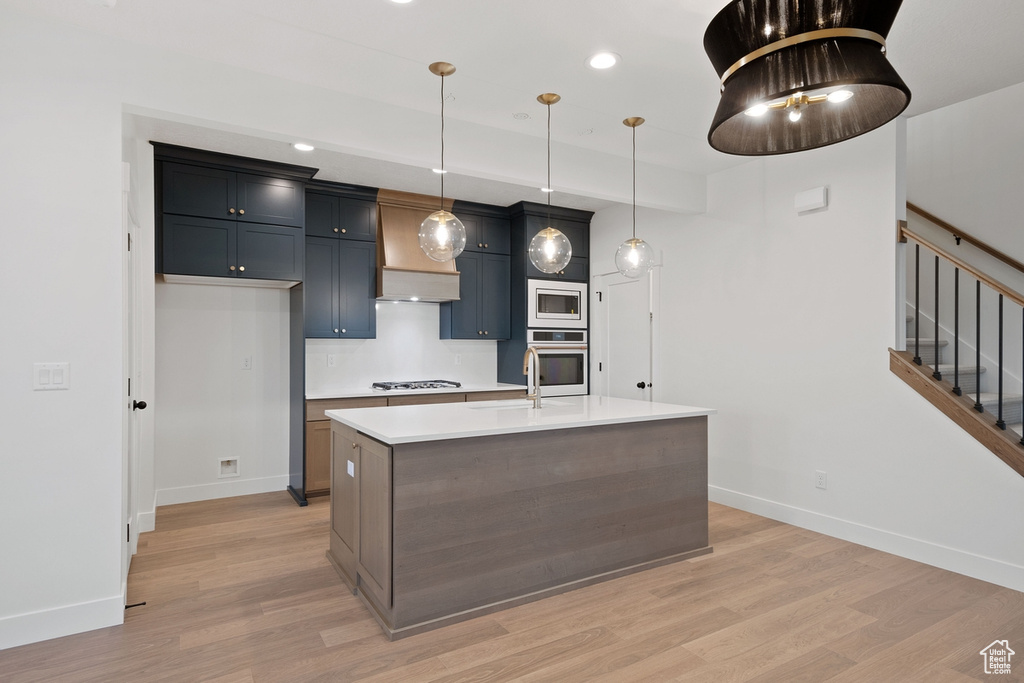 Kitchen featuring stainless steel microwave, oven, baseboards, light wood-style floors, and recessed lighting