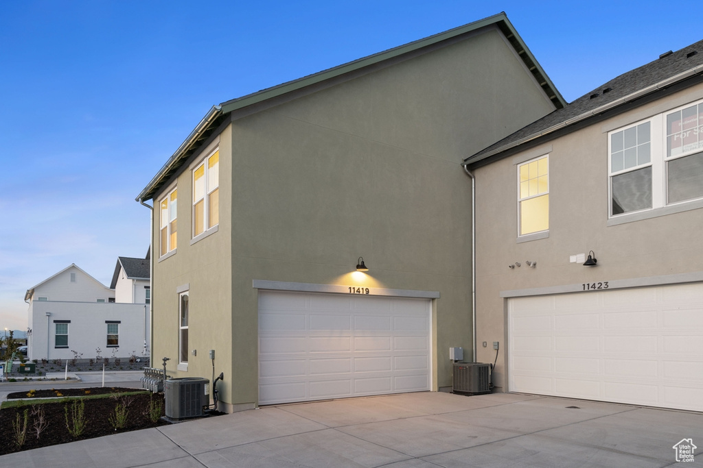 View of side of home with a garage, stucco siding, concrete driveway, and central air condition unit