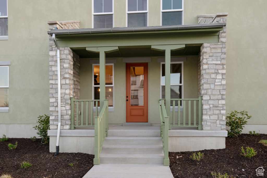 View of exterior entry with stucco siding, stone siding, and covered porch