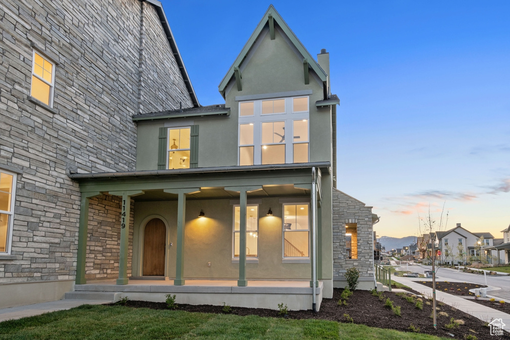 Back of house at dusk with covered porch, stone siding, and stucco siding