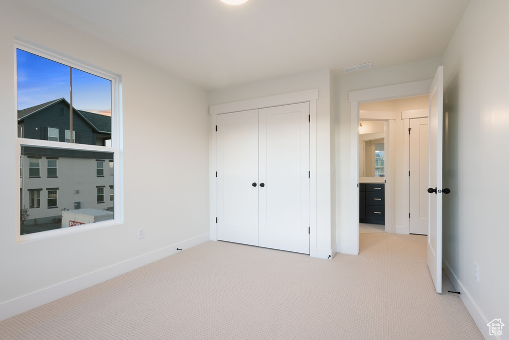 Unfurnished bedroom featuring light carpet, baseboards, a closet, and multiple windows