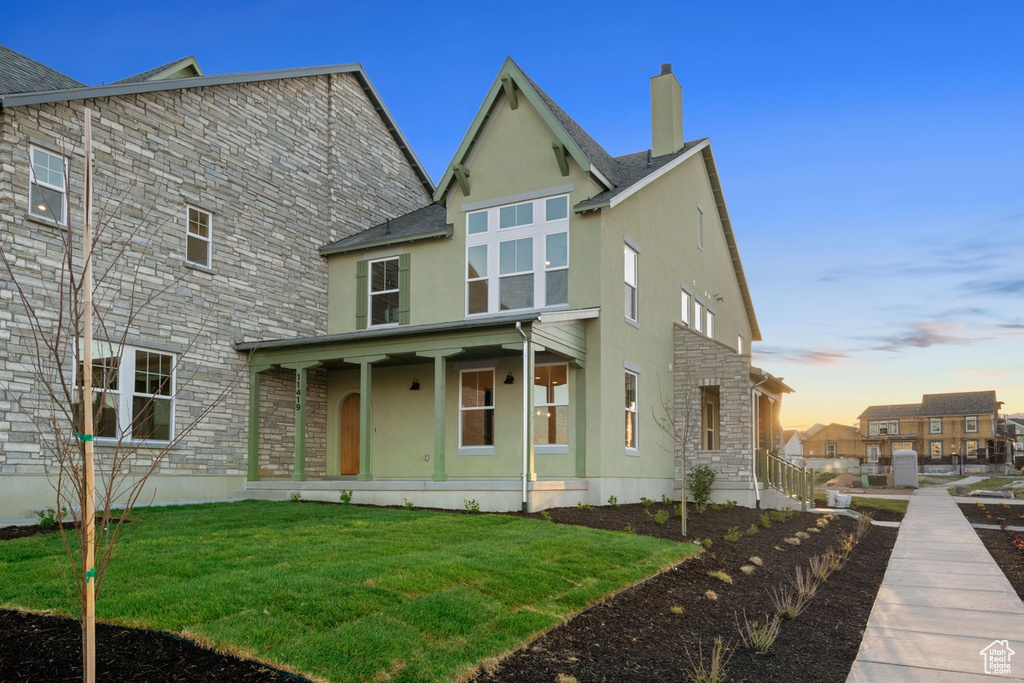 Rear view of property featuring stone siding, stucco siding, a porch, a lawn, and a chimney