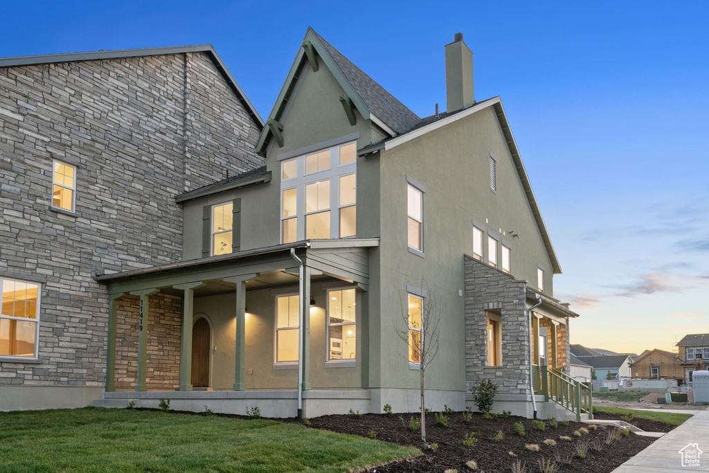 Back of property at dusk featuring stone siding, stucco siding, a chimney, and a yard