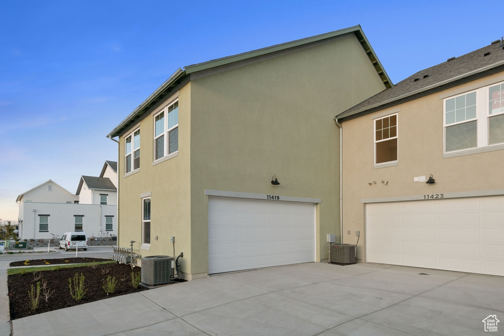 View of side of home with a garage, stucco siding, cooling unit, and driveway