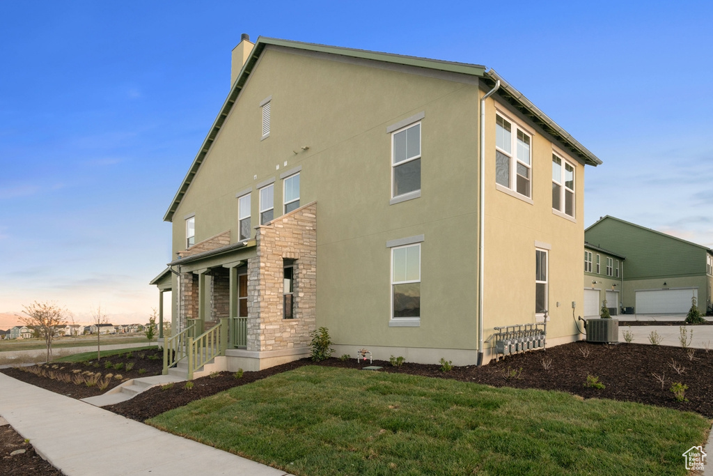 Property exterior at dusk featuring stucco siding, a chimney, a yard, stone siding, and central air condition unit