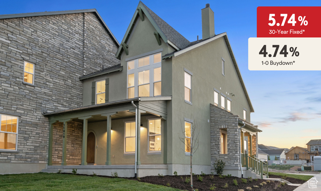 Back of house at dusk with stone siding, stucco siding, and a porch