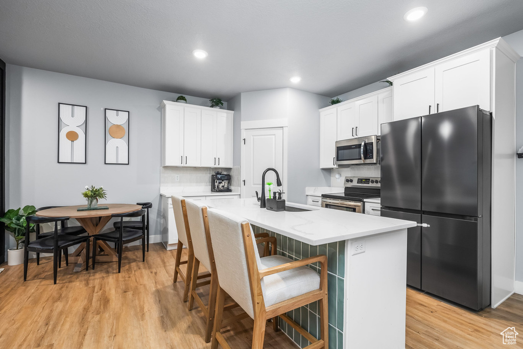 Kitchen featuring appliances with stainless steel finishes, a sink, light wood-style flooring, backsplash, and light countertops