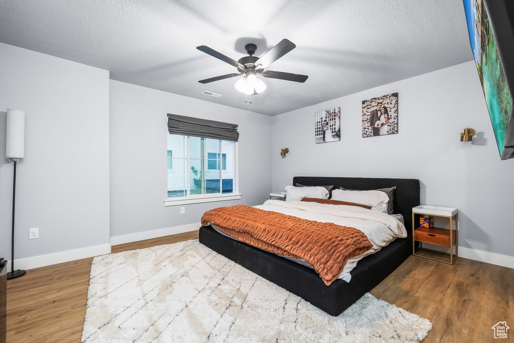 Bedroom with baseboards, wood finished floors, ceiling fan, and a textured ceiling