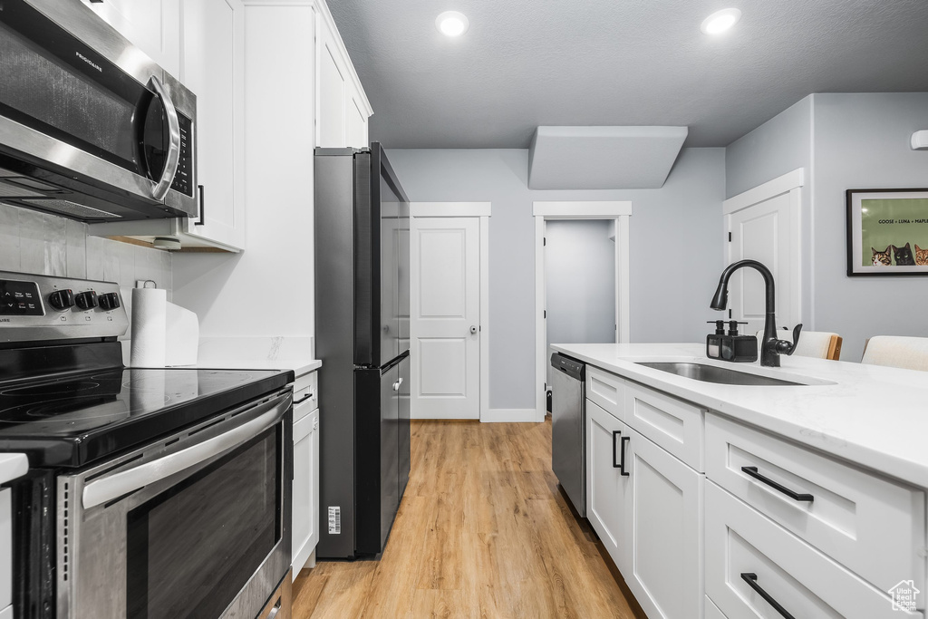 Kitchen with appliances with stainless steel finishes, a sink, white cabinets, light wood-style floors, and recessed lighting