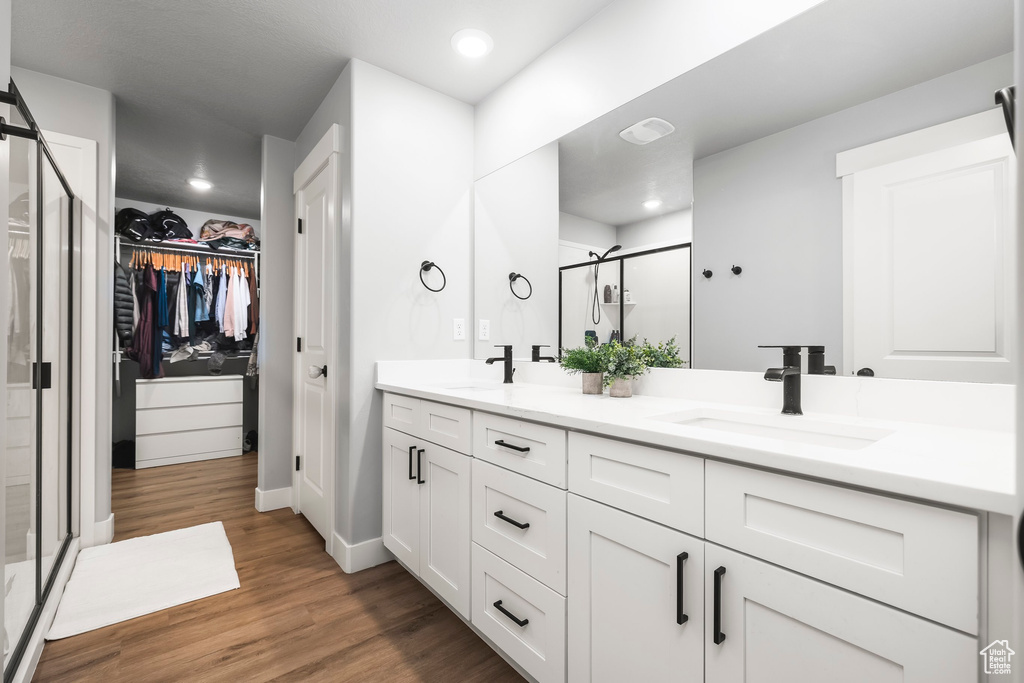Bathroom with a shower stall, double vanity, a walk in closet, wood finished floors, and recessed lighting