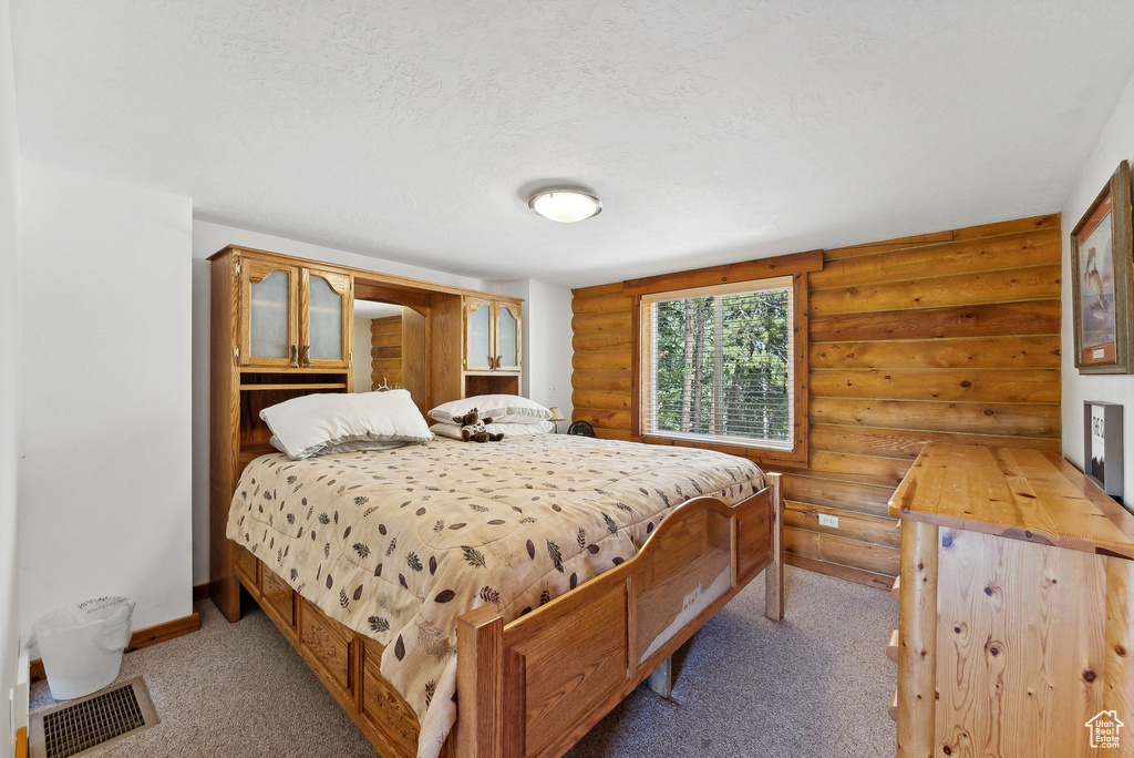Bedroom featuring rustic walls, light colored carpet, baseboards, and a textured ceiling