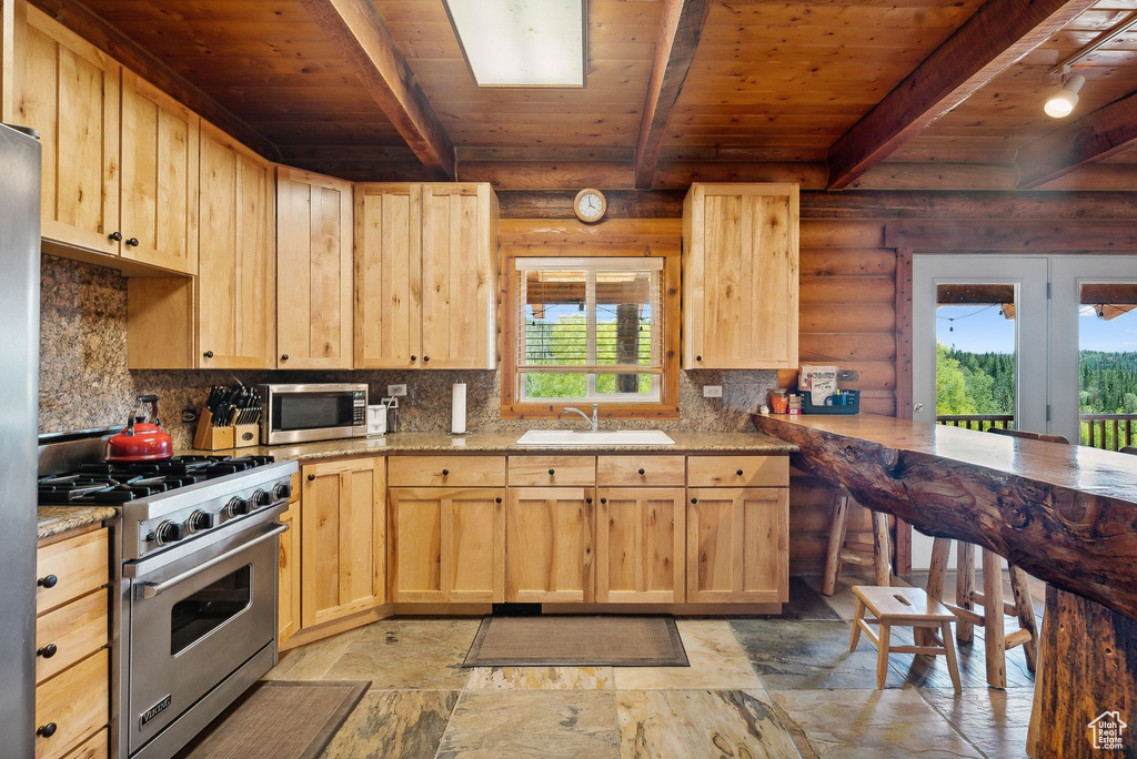 Kitchen featuring appliances with stainless steel finishes, light brown cabinets, rustic walls, wood ceiling, and a sink