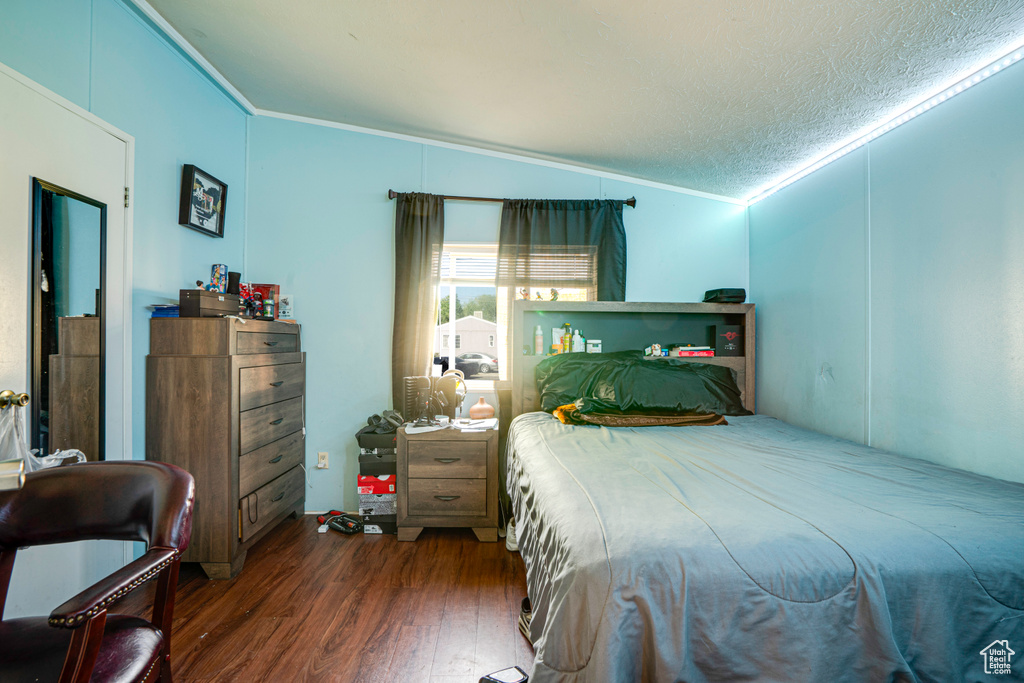 Bedroom featuring ornamental molding, wood finished floors, lofted ceiling, and a textured ceiling