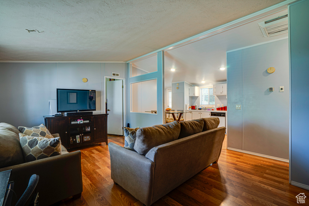 Living area with wood finished floors, a textured ceiling, vaulted ceiling, and crown molding