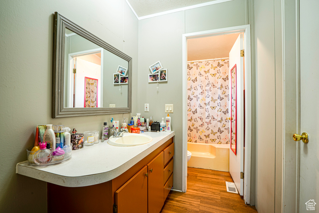 Bathroom with wood finished floors, vanity, toilet, and shower / bathtub combination with curtain