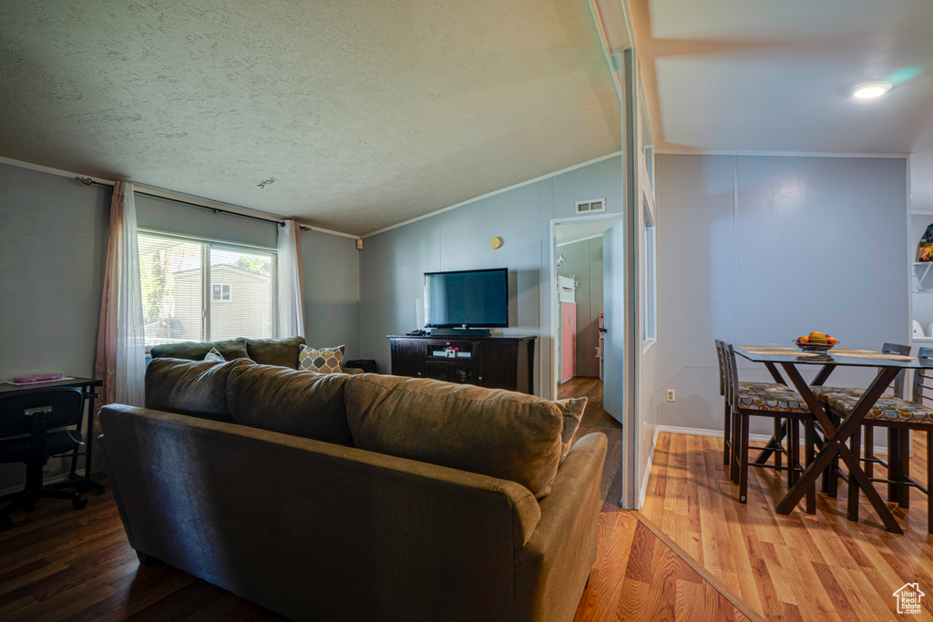 Living area with crown molding, vaulted ceiling, light wood-type flooring, and a textured ceiling