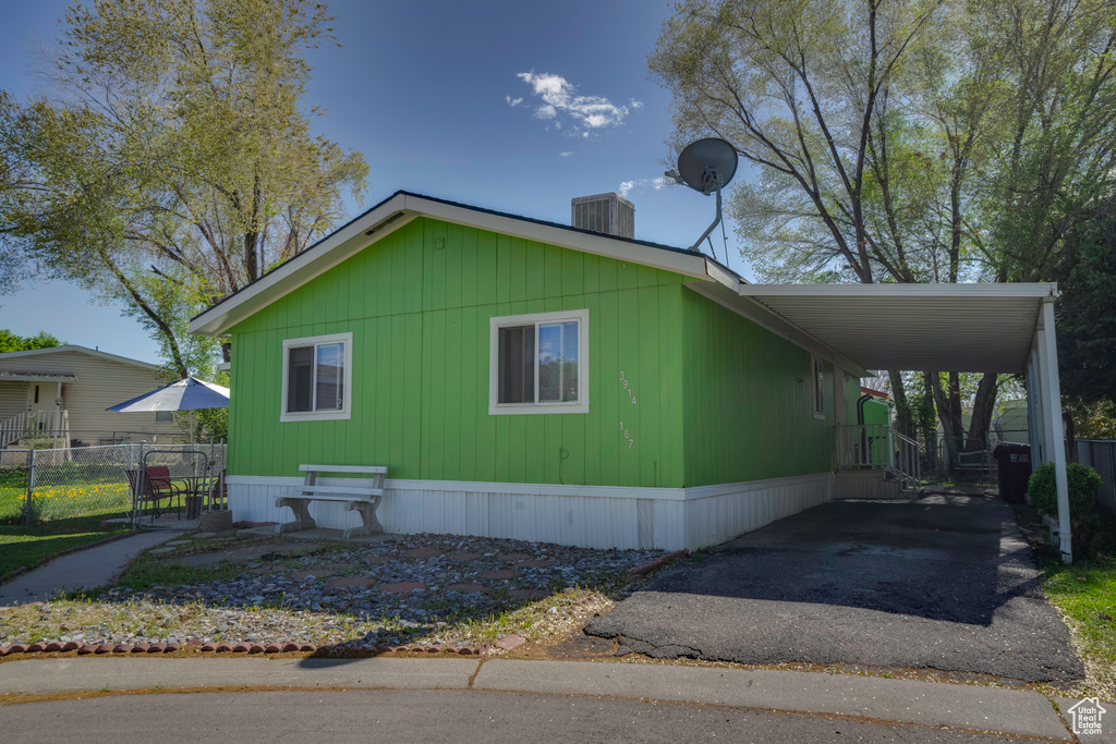 View of property exterior with asphalt driveway, a carport, fence, and central AC