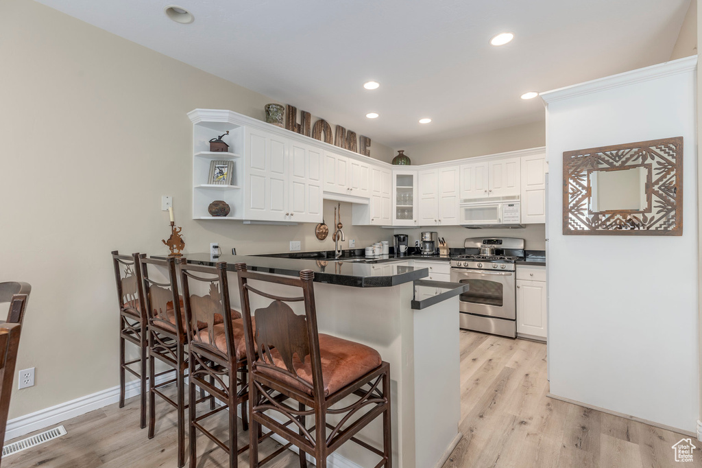 Kitchen with stainless steel gas stove, white microwave, a breakfast bar, a peninsula, and white cabinetry