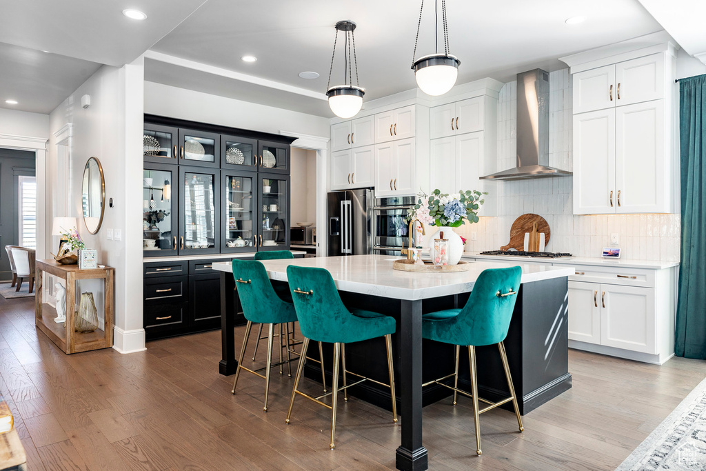 Kitchen featuring wall chimney exhaust hood, high quality fridge, light countertops, and recessed lighting
