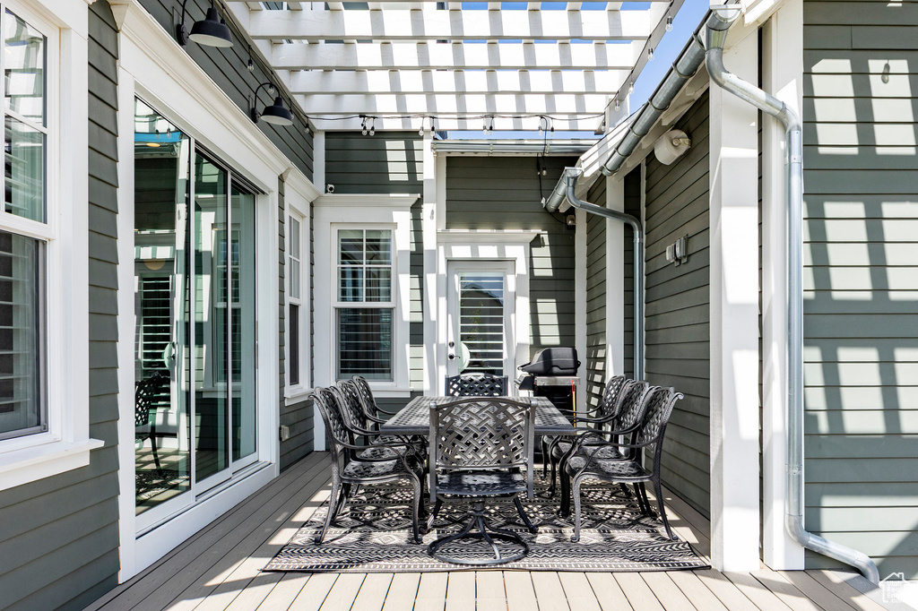 Wooden deck featuring outdoor dining space, a pergola, and a grill