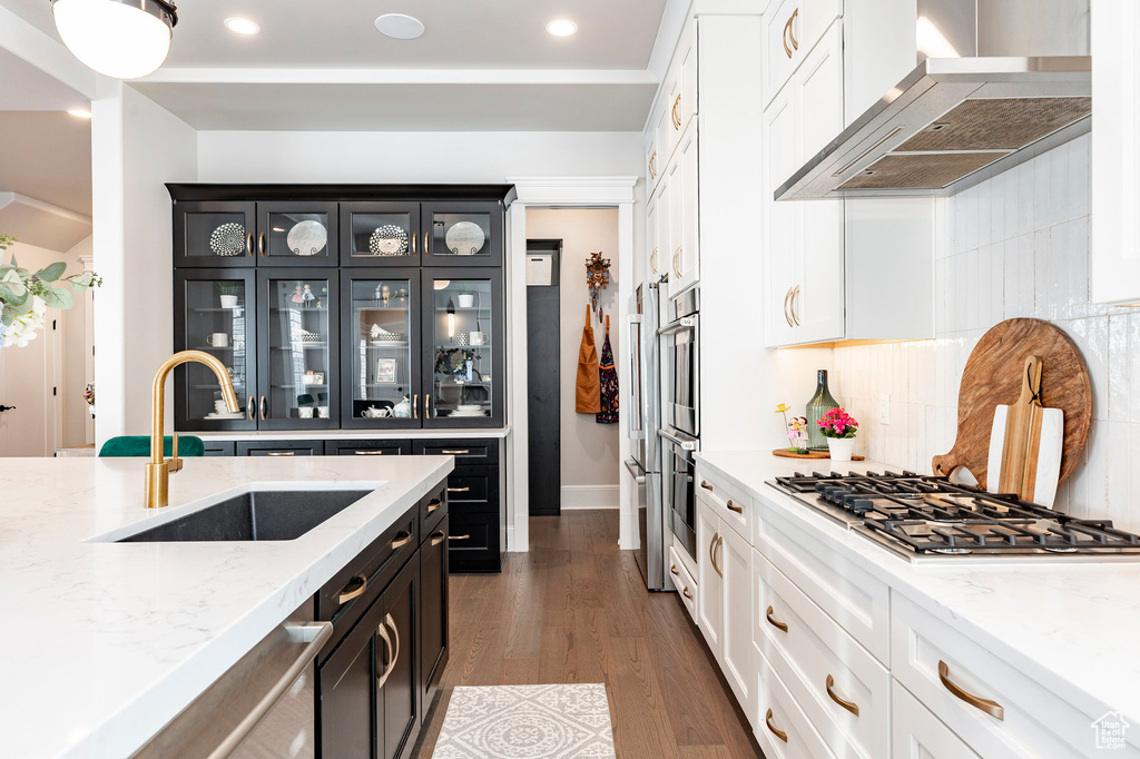 Kitchen with wall chimney range hood, a sink, appliances with stainless steel finishes, dark cabinets, and recessed lighting