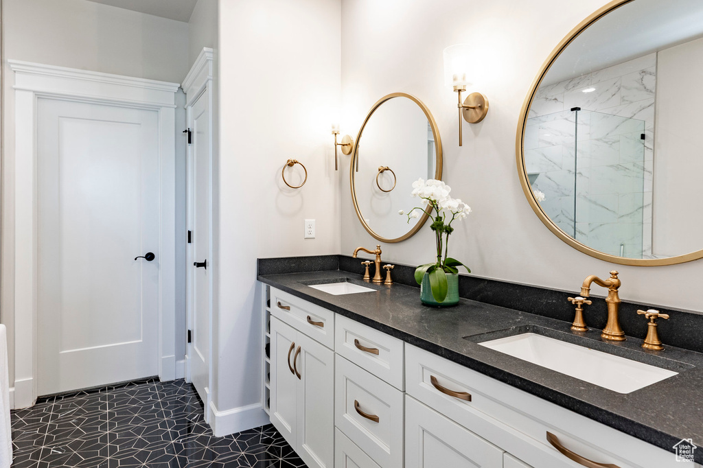 Bathroom with a marble finish shower, double vanity, tile patterned floors, and baseboards