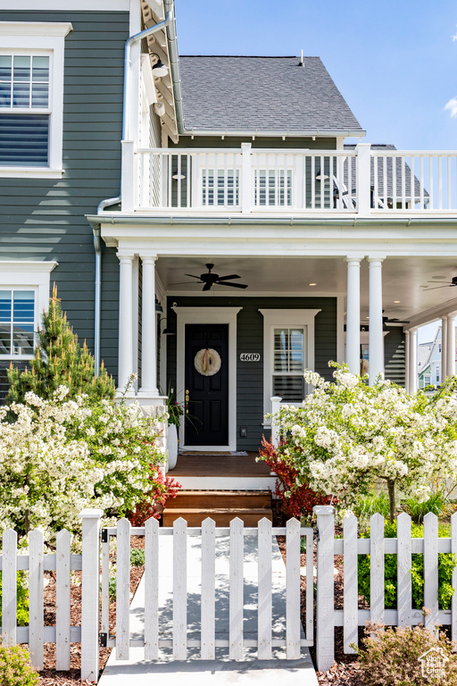 View of front of home featuring a balcony, ceiling fan, covered porch, a fenced front yard, and a gate