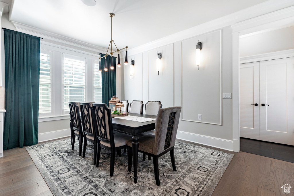 Dining room with a chandelier, wood finished floors, baseboards, and crown molding