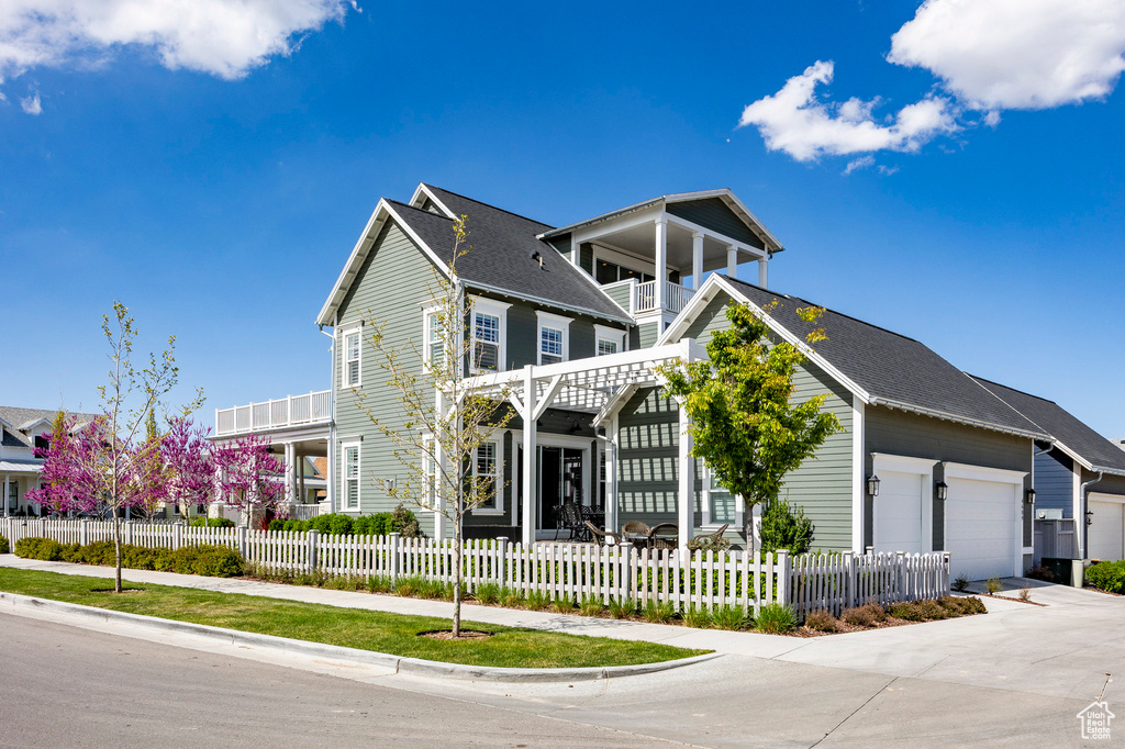 View of front facade featuring a balcony, a garage, a fenced front yard, and driveway