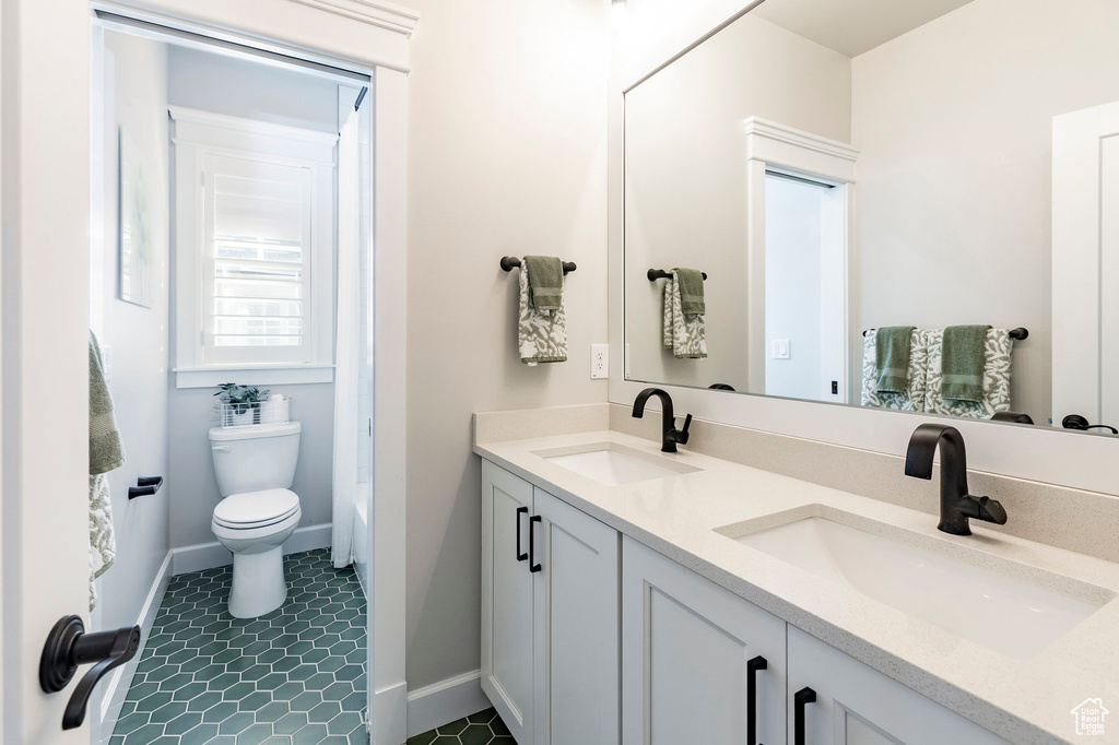 Bathroom featuring toilet, double vanity, baseboards, and a shower