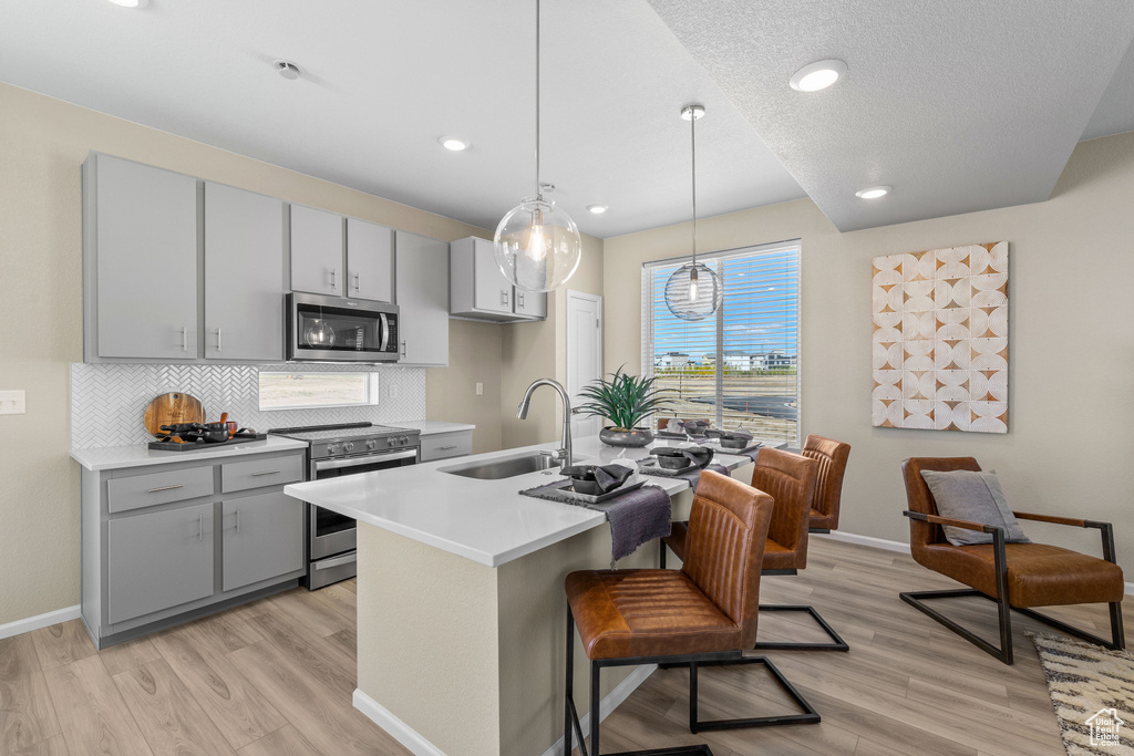 Kitchen with appliances with stainless steel finishes, a sink, gray cabinets, light wood-style floors, and recessed lighting