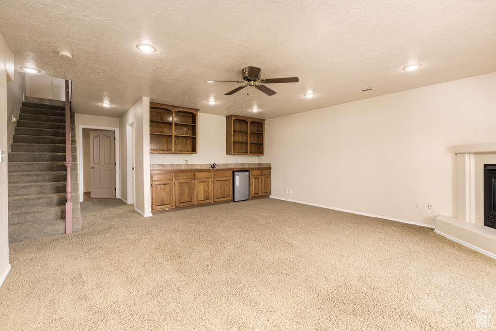 Unfurnished living room with wet bar, baseboards, light carpet, recessed lighting, and stairs