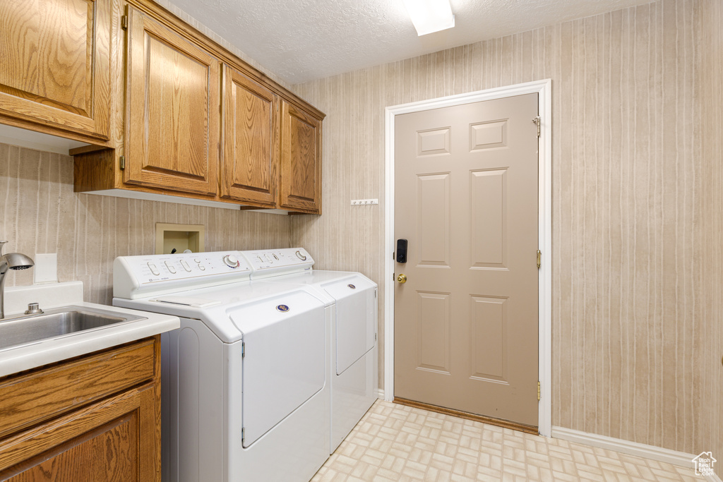 Laundry area with wallpapered walls, washer and dryer, cabinet space, a textured ceiling, and baseboards