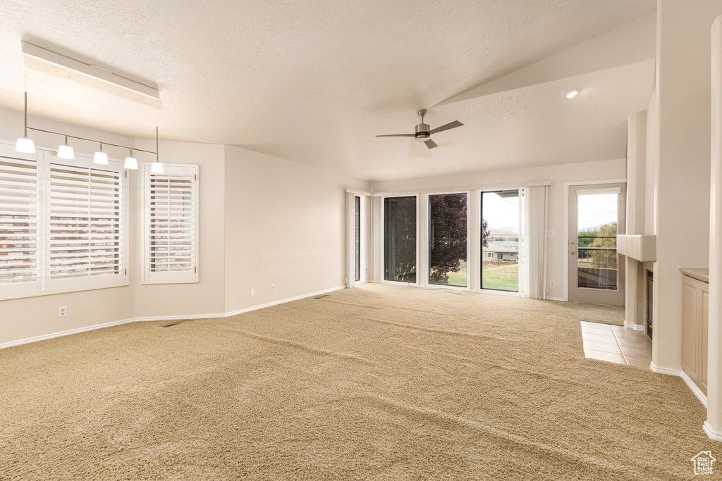 Carpeted spare room featuring ceiling fan, baseboards, vaulted ceiling, and a textured ceiling