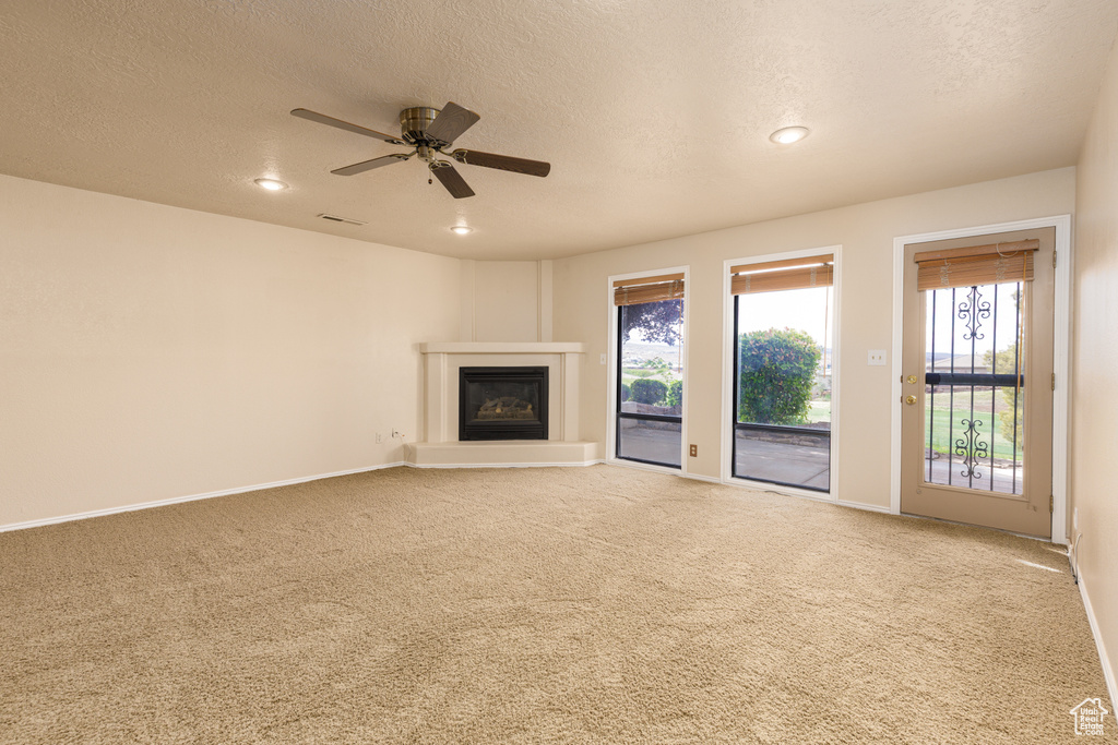 Unfurnished living room with carpet, a textured ceiling, a glass covered fireplace, plenty of natural light, and recessed lighting