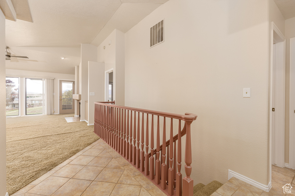 Hall with an upstairs landing, light colored carpet, vaulted ceiling, light tile patterned floors, and baseboards