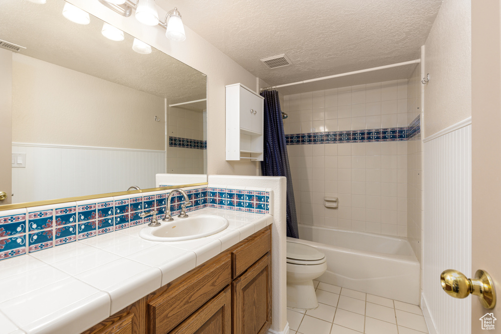 Bathroom with tile patterned floors, toilet, shower / bathtub combination with curtain, a wainscoted wall, and vanity