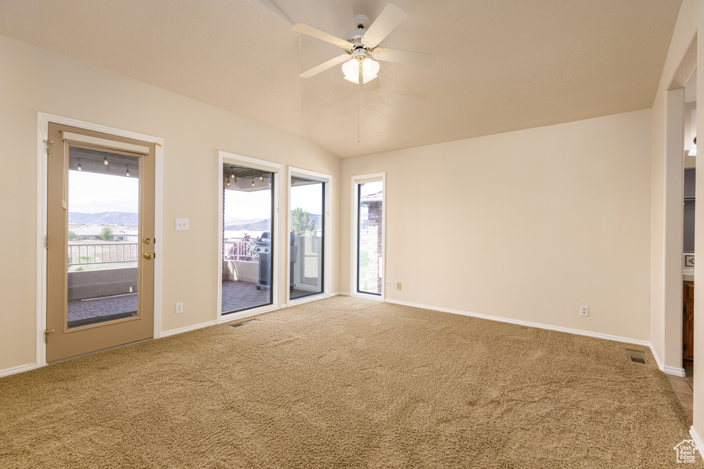 Carpeted spare room featuring a ceiling fan, vaulted ceiling, and baseboards