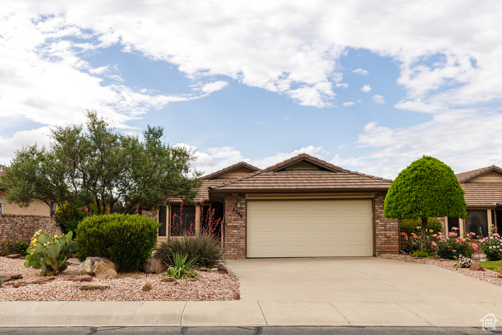 Ranch-style house with an attached garage, driveway, brick siding, and a tiled roof