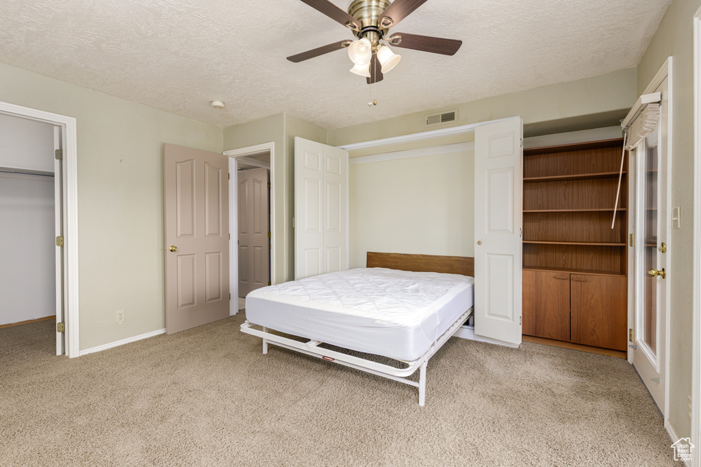 Carpeted bedroom with a textured ceiling, baseboards, a ceiling fan, and a closet