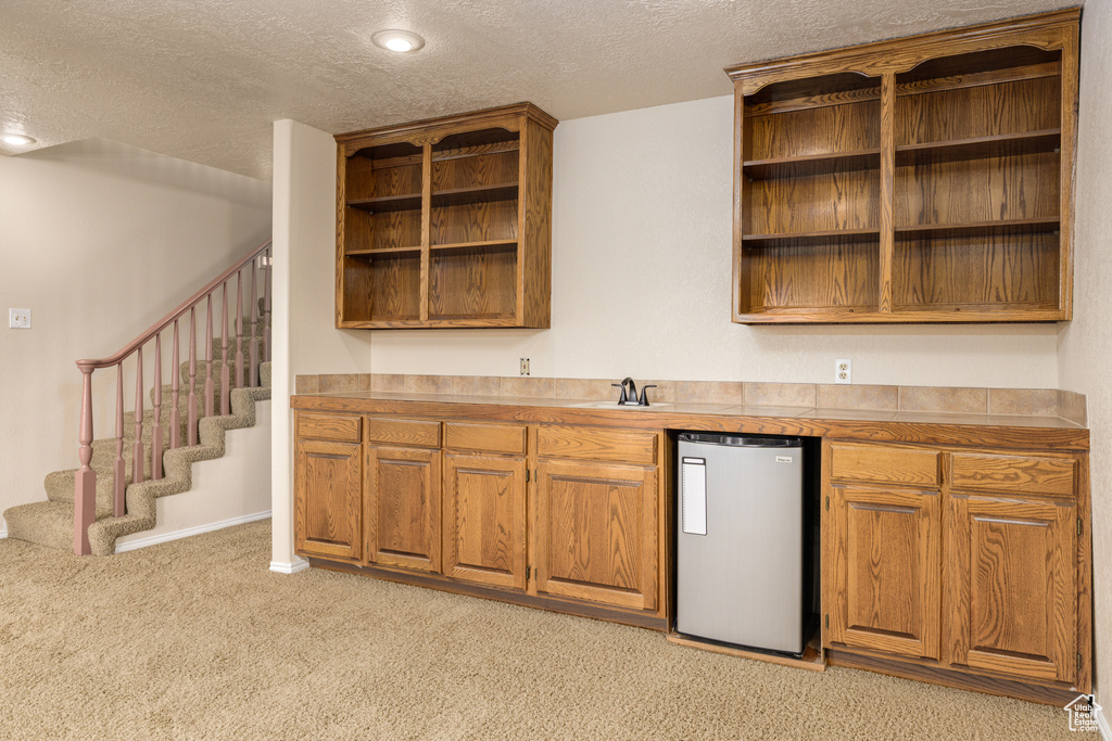 Kitchen featuring open shelves, a textured ceiling, freestanding refrigerator, light carpet, and brown cabinets
