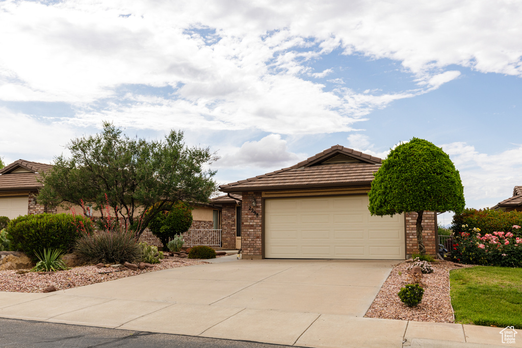 Single story home with a tile roof, concrete driveway, brick siding, and a garage