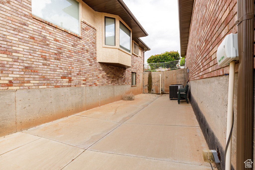 View of side of home with cooling unit, brick siding, a patio area, fence, and stucco siding