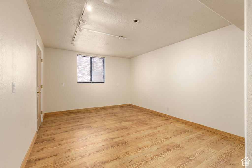 Empty room with a textured ceiling, light wood-style flooring, rail lighting, and baseboards